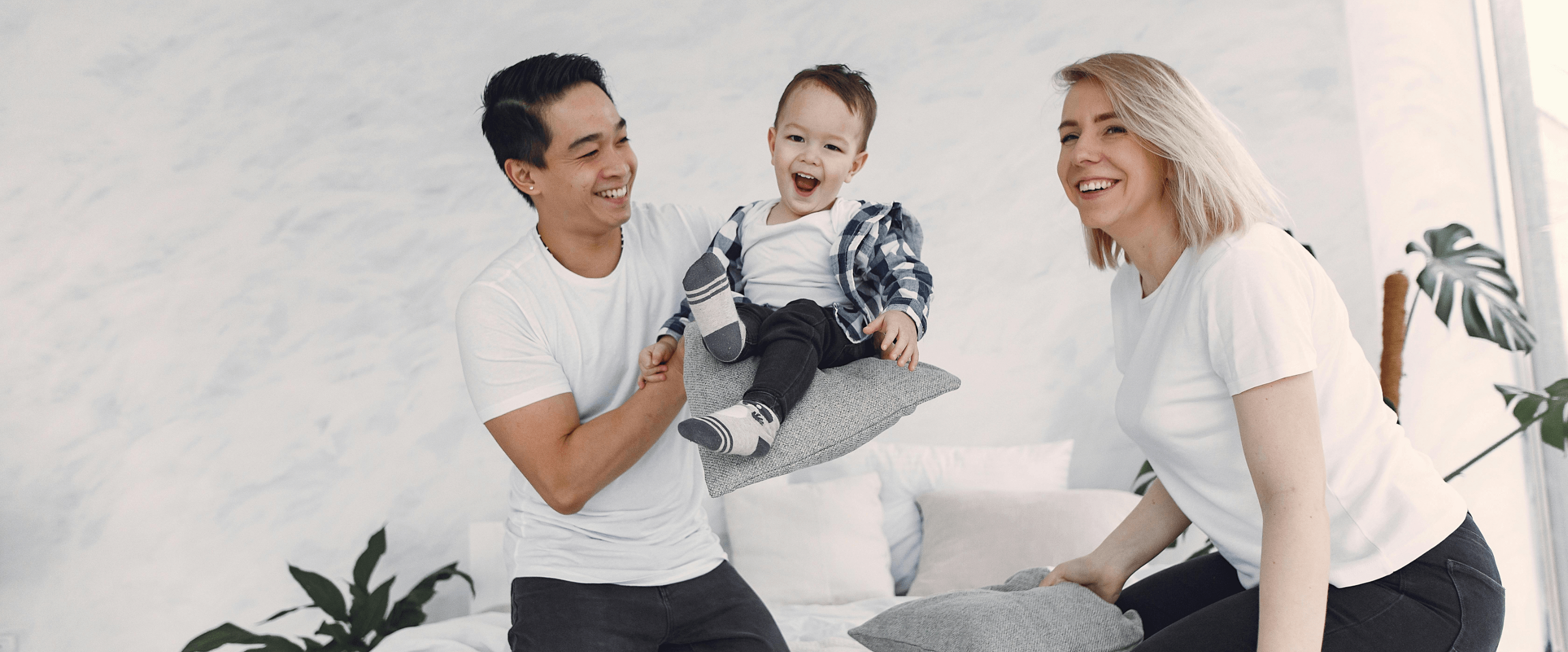 Familie sitzt auf einem Bett und spielt mit Kissen